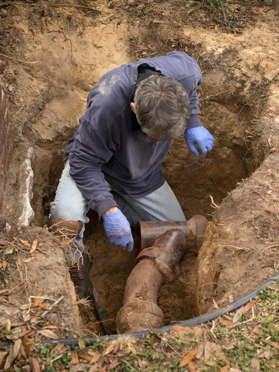 Engineer kneeling in a dug-out pit in a garden beside an old salt-glazed clay drain junction