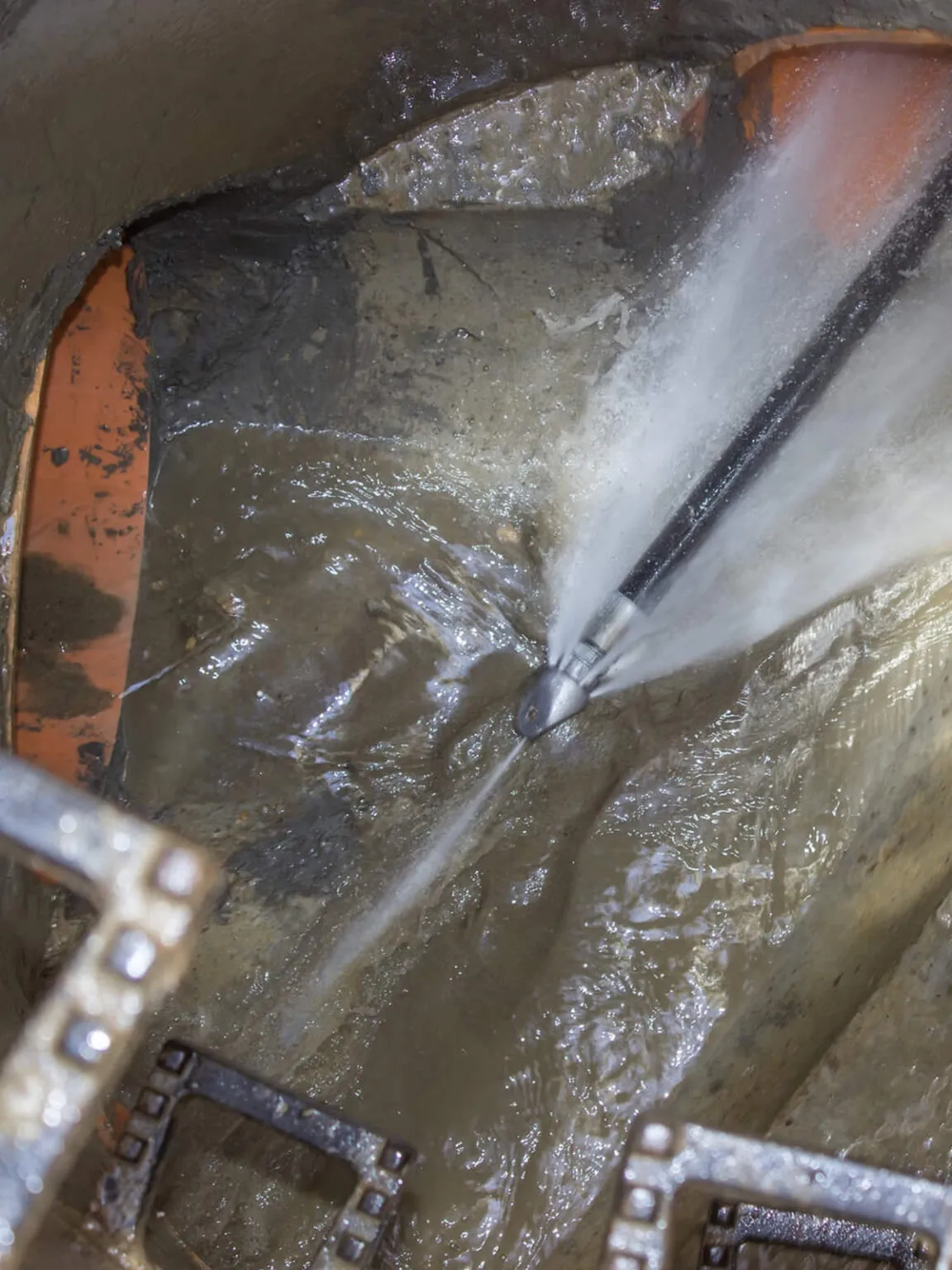 Jetting nozzle spraying water inside a drain chamber and cutting silt off the pipe wall