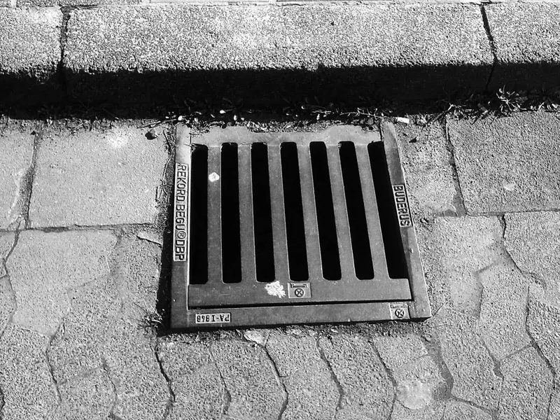 Black-and-white photo of a plain drain grating set in stone paving, Derby DE22