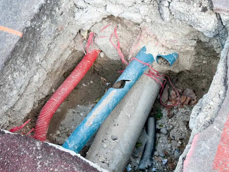 Road excavation showing a red corrugated conduit, a blue pipe and a grey pipe with loose cabling, Derby DE24