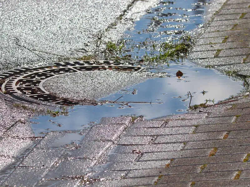 Solid manhole cover set in block paving with rainwater pooling around it