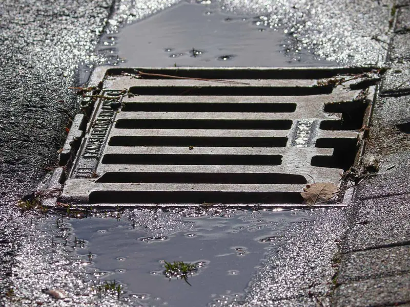 Cast iron gully grating in a block-paved yard with water pooling around it
