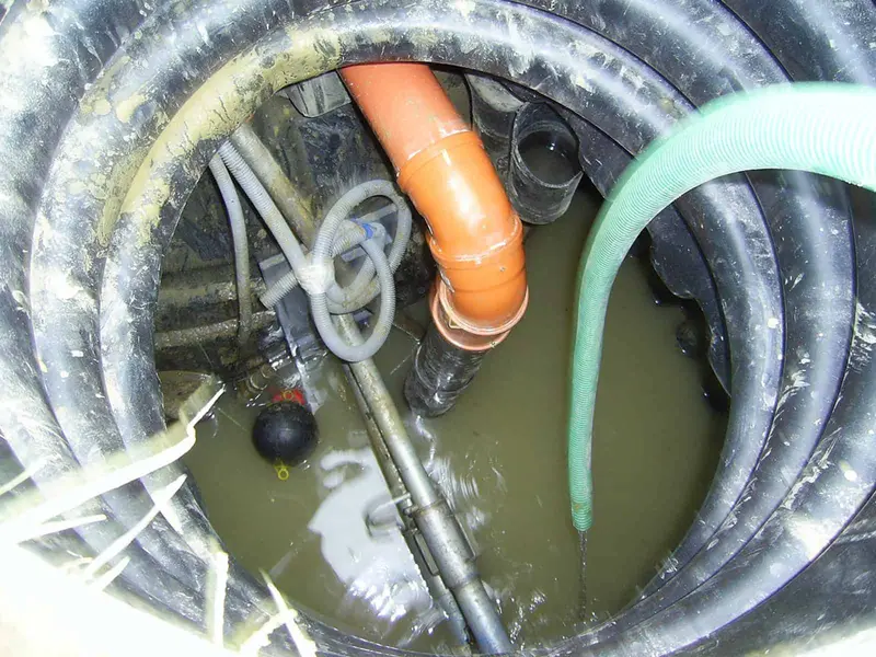 Looking down into an open tank chamber with an orange inlet pipe, float switches and a suction hose in the liquid