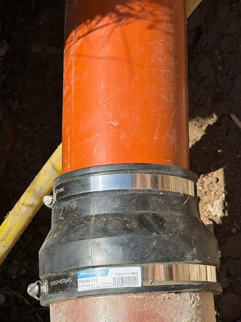 New orange plastic drain pipe joined to the old pipe with a rubber coupling in a trench at a city centre property in Derby
