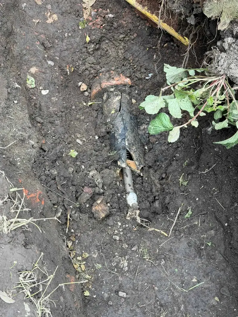Cracked drain pipe exposed in a garden trench in Littleover, with a threaded metal rod lying in the broken section