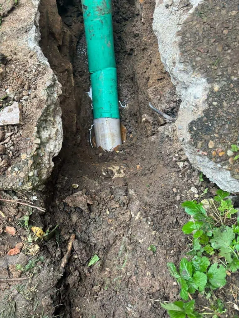 Green plastic pipe laid in a narrow trench cut through a concrete path at a house in Mickleover