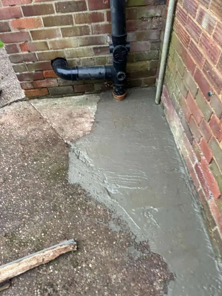 Fresh concrete laid around the foot of a black soil pipe in the corner of a yard at a house in Sinfin