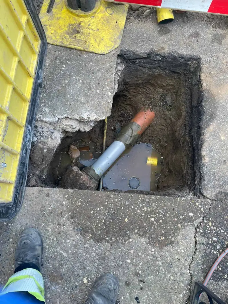 New pipe section coupled into the old clay drain in a small excavation beneath a lifted road plate at a property in Mickleover