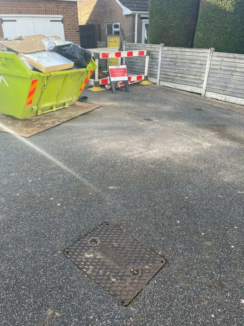 Loaded skip and a barrier board beside a closed steel access cover on a driveway, Mickleover DE3