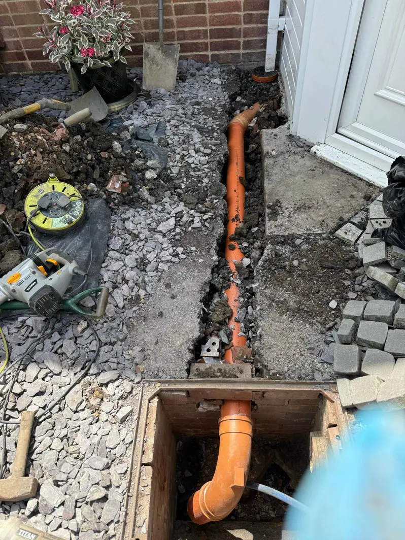 New orange plastic drain pipe laid in an open trench to a new inspection chamber beside a house door in Sinfin, Derby DE24